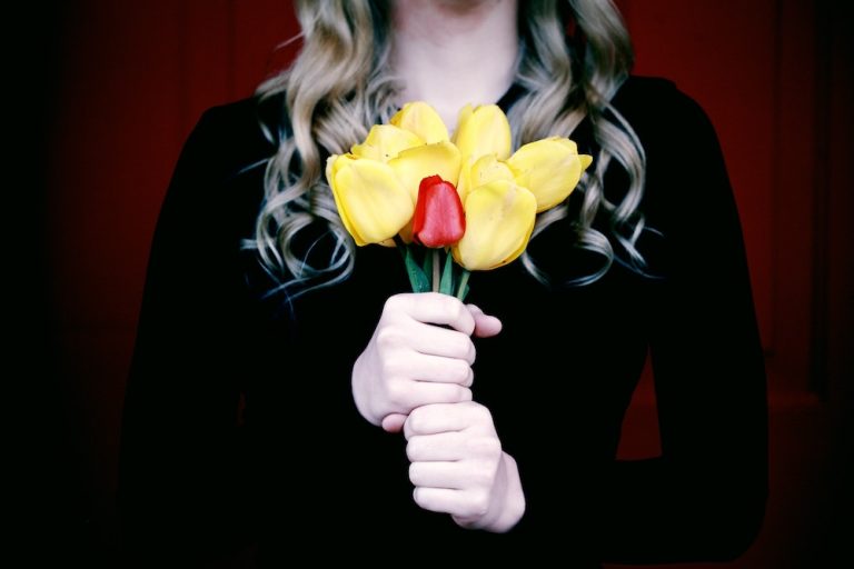 Woman holding a bouquet of yellow roses and one red rose