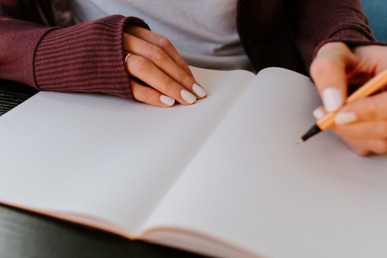 A woman in a red cardigan and gray shirt writes in an empty notebook