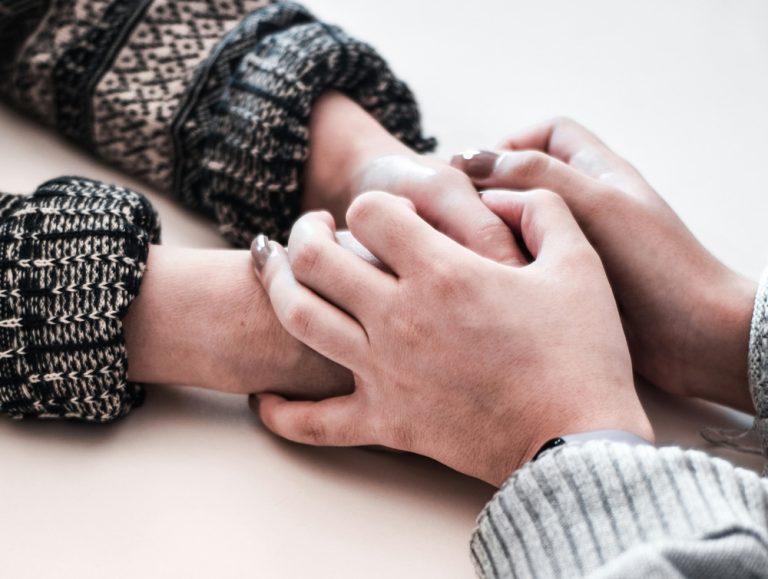 A person in a black sweater and a person in a gray sweater hold hands over a table